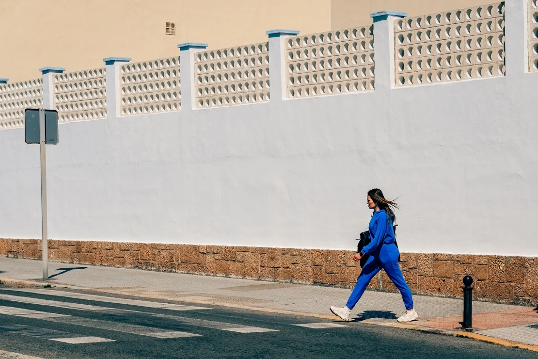 Frau in blau geht in Cadiz vor einer weißen Wand über die Straße